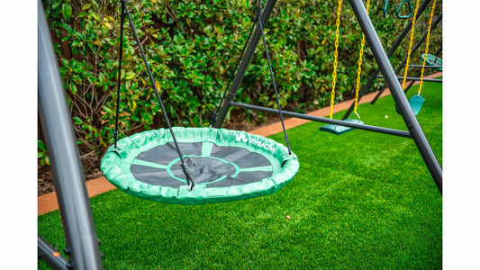A green platform swing next to two other swings on a large metal swing set.