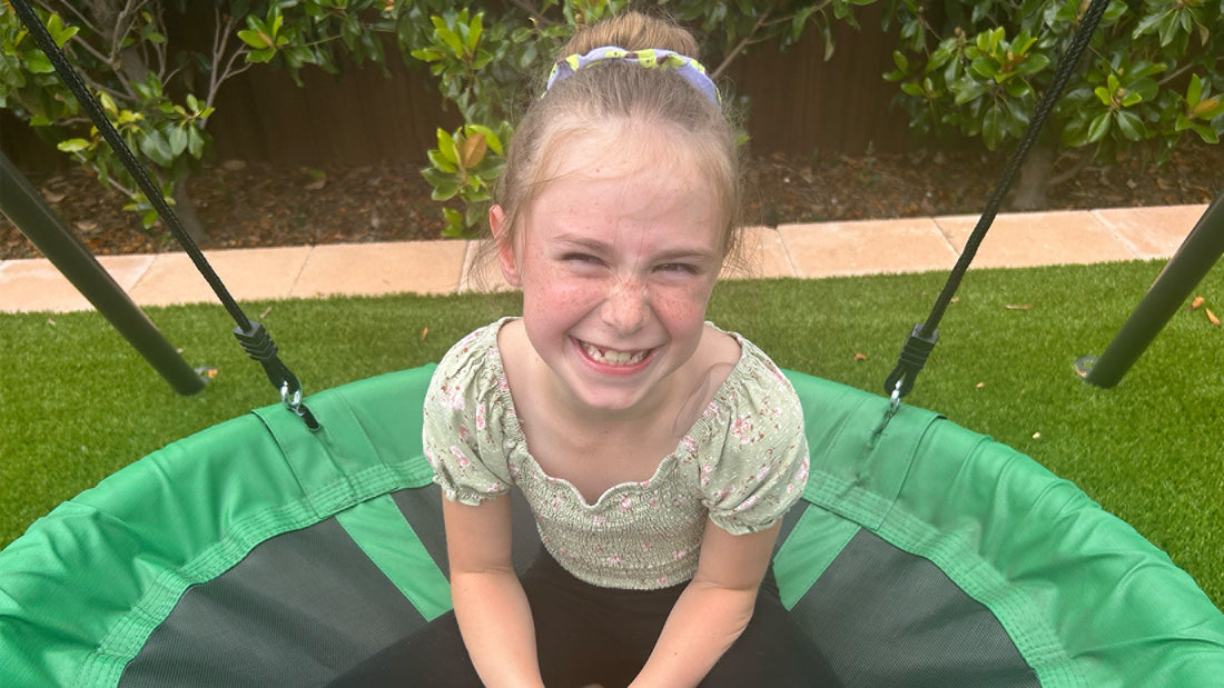 A smiling girl sitting on the gobaplay Round Platform Tree Swing.