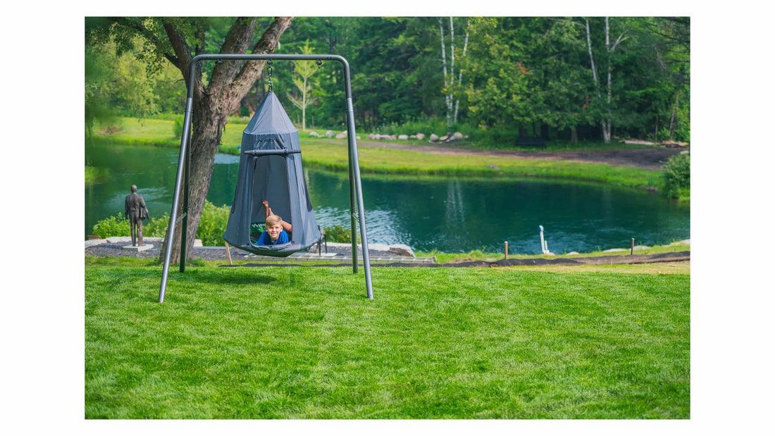 A boy laying in a grey tent swing in a pretty backyard. 